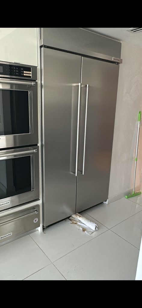 Before: Stainless steel refrigerator with clutter on kitchen floor